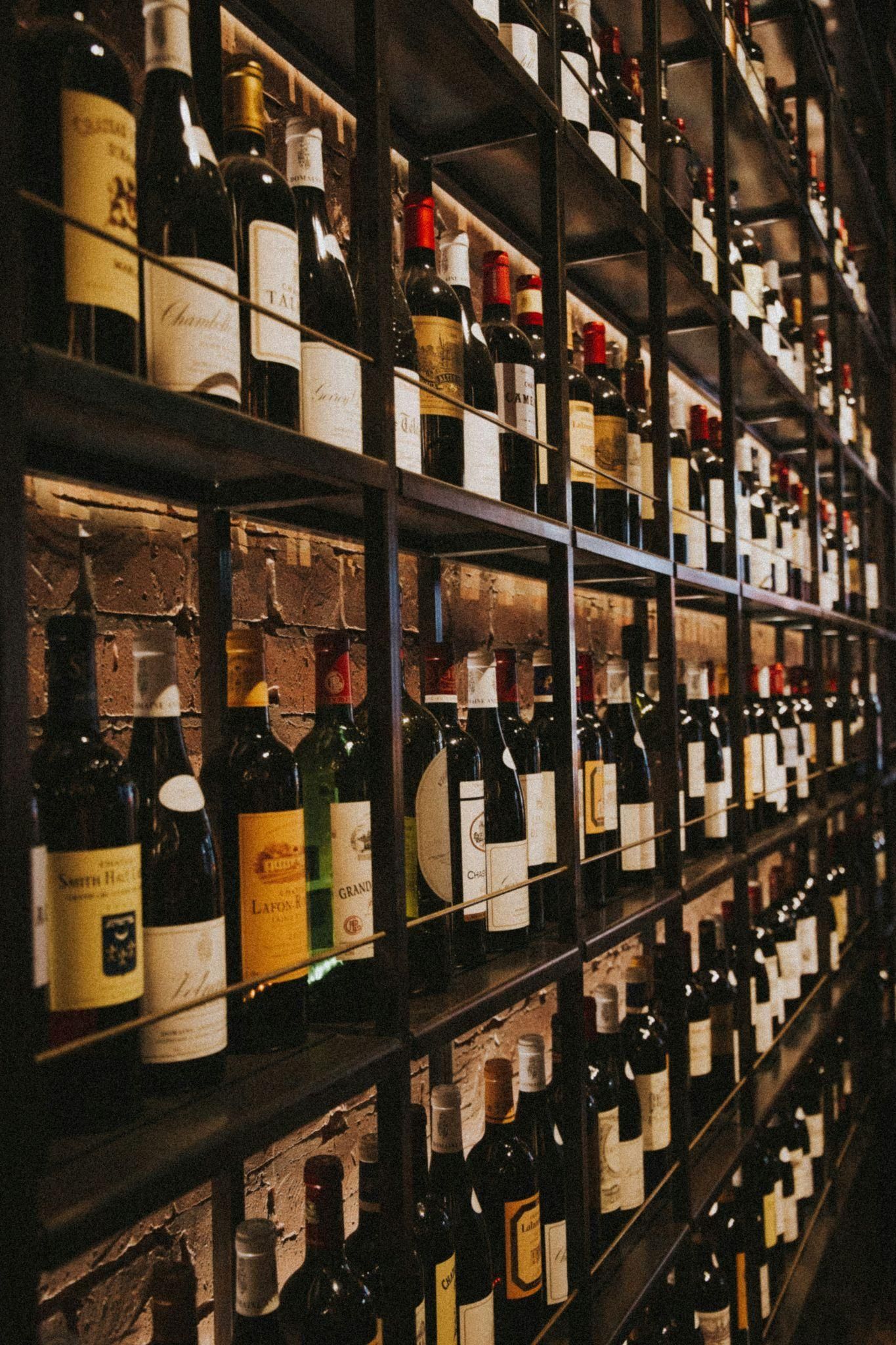 A backlit shelving unit in front of a brick wall displaying hundreds of wine bottles