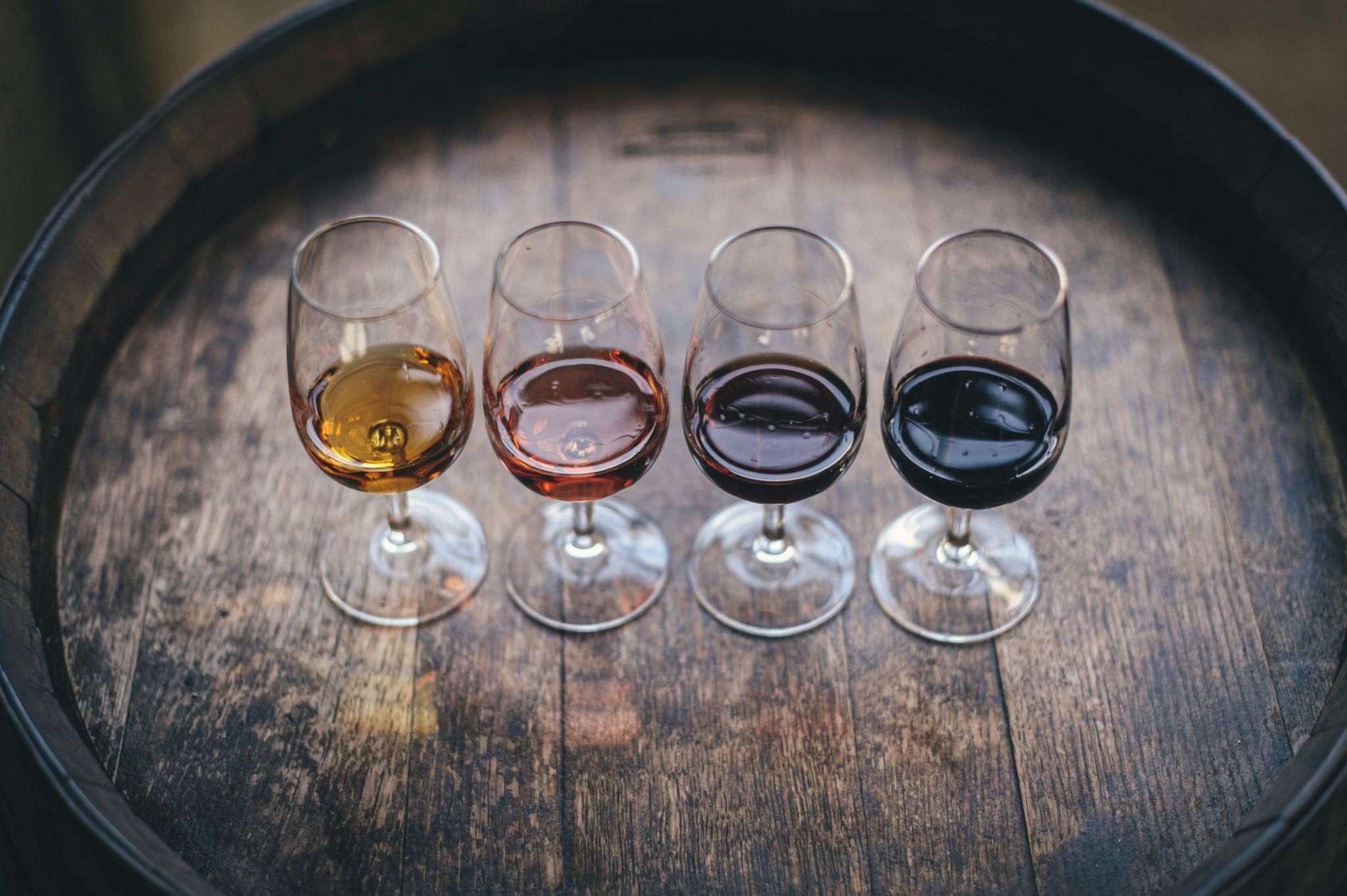 Four wine glasses containing different types of wine lined up on top of a wooden barrel