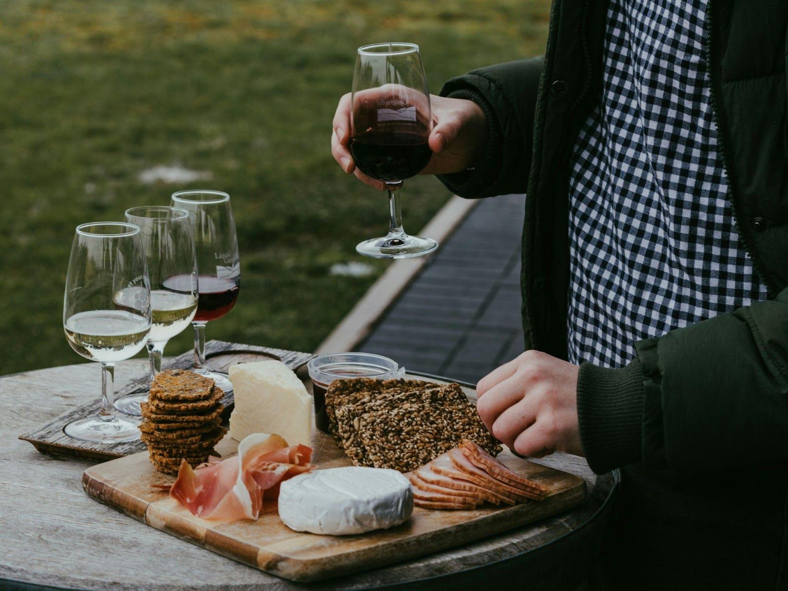 A person holding a glass of wine, picking from a board of charcuterie, cheese and crackers