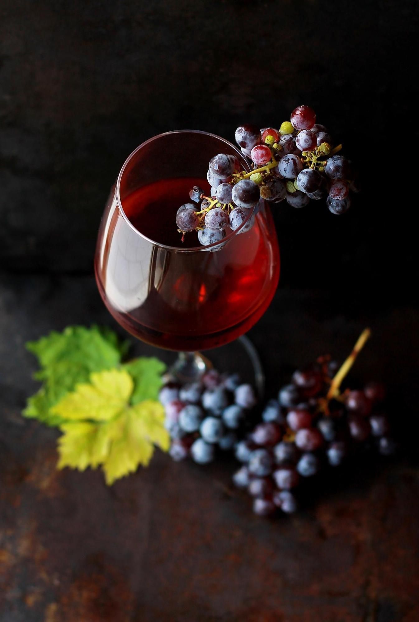 A elegant glass of red wine accompanied by a bunch of fresh grapes, capturing the essence and origins of the wine