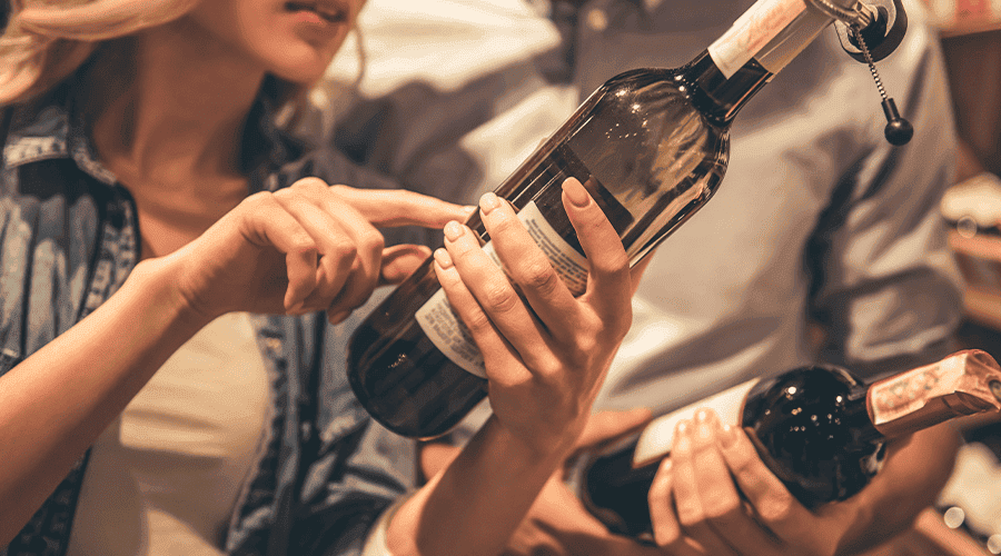 Two individuals examining and discussing bottles of wine.